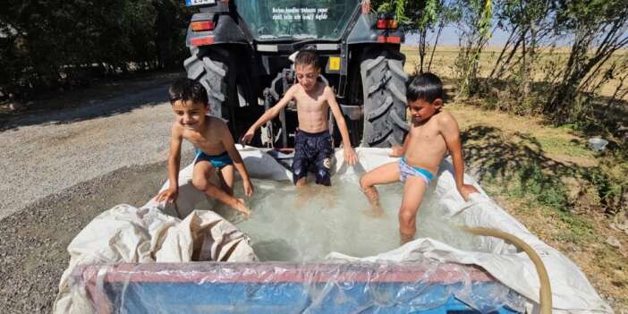 Traktörün arkasındaki su dolu sepette serinlediler